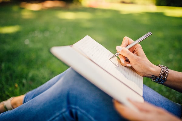 woman writes in a journal outside