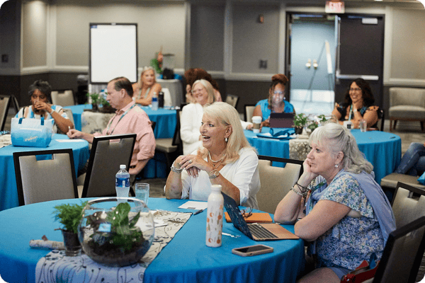 conference attendees sit at tables listening in to a keynote speaker