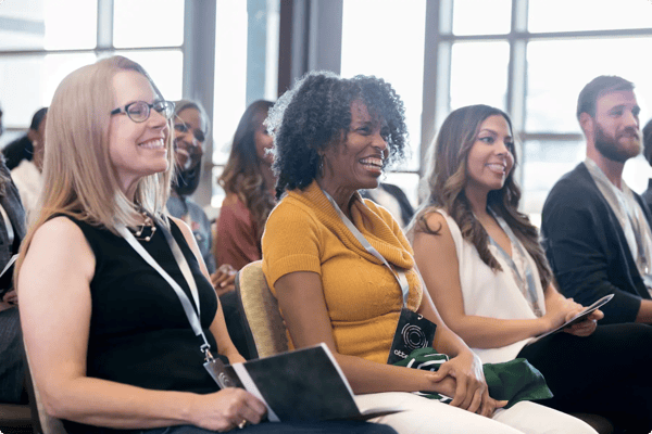 three women smile as they watch a keynote speaker