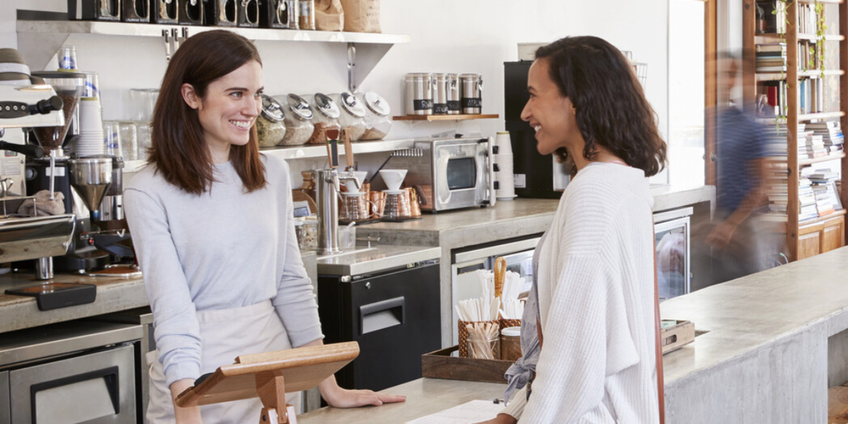 a smiling female coffee shop cashier takes the order of a female customer
