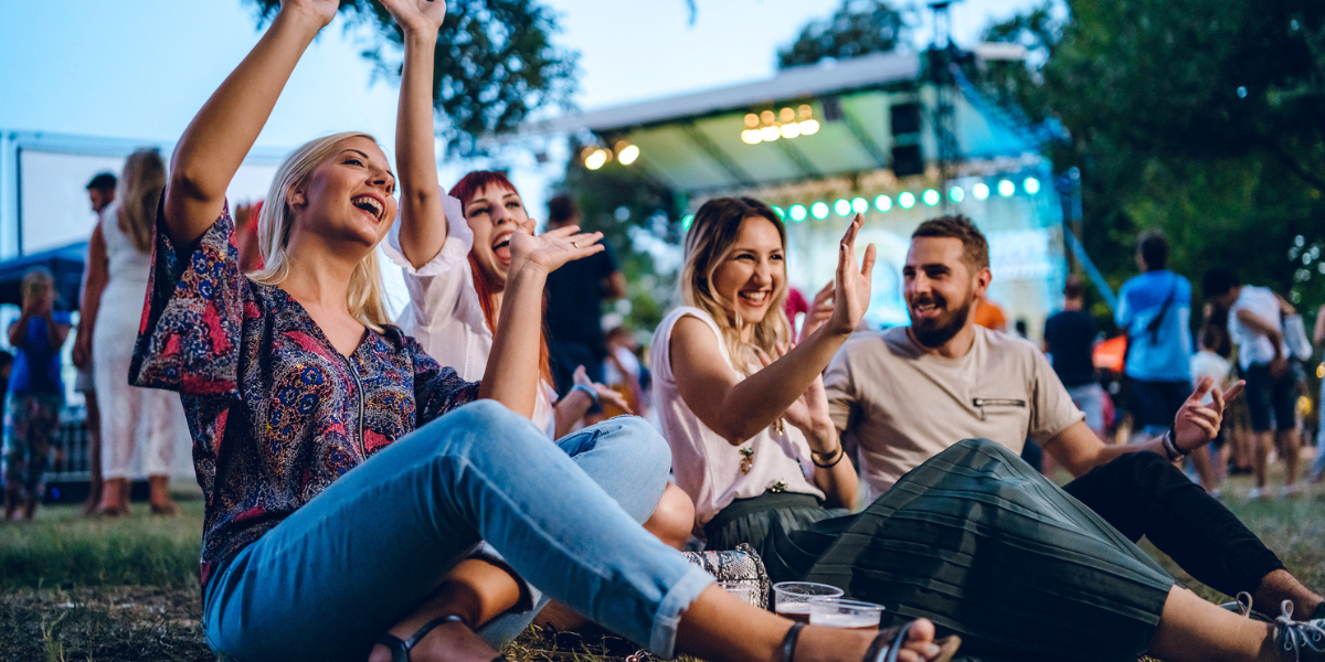 Three women and a man sitting on the ground at an outdoor summer concert