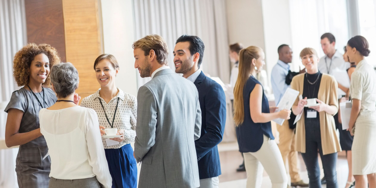 Twelve business professionals smile, drink coffee, and network in a brightly lit convention center room