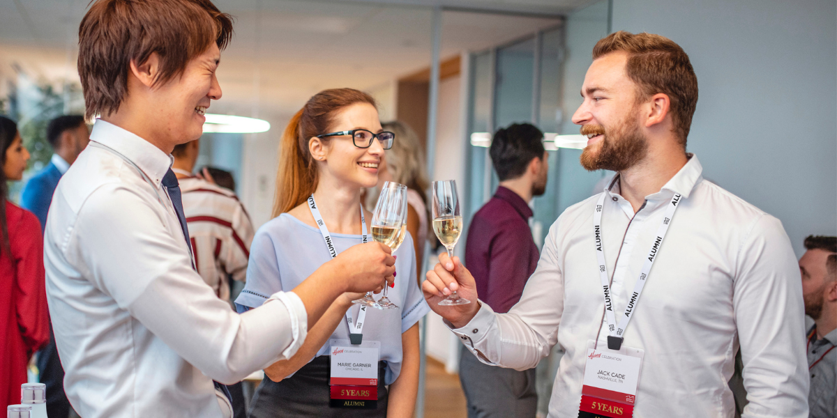 three alumni event attendees wearing badges and drinking champagne