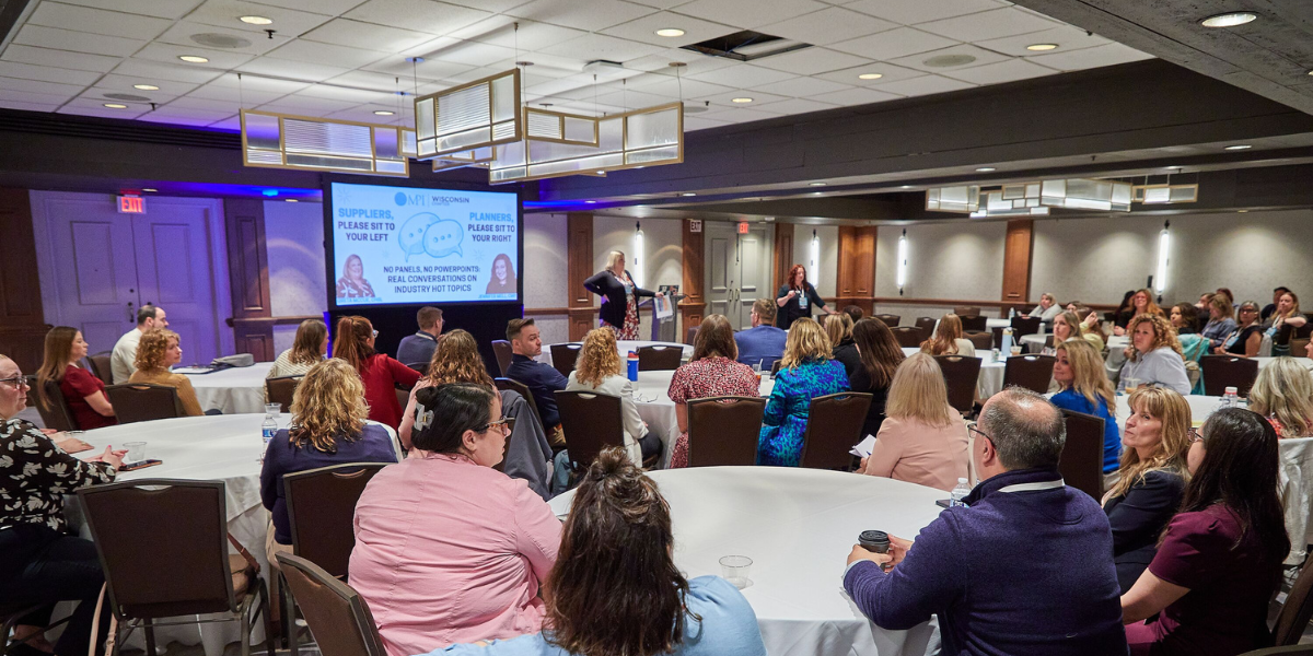 A crowd of attendees sits in a breakout session room at a conference