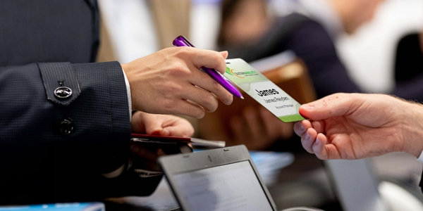 A male registration desk worker offers a woman her event badge