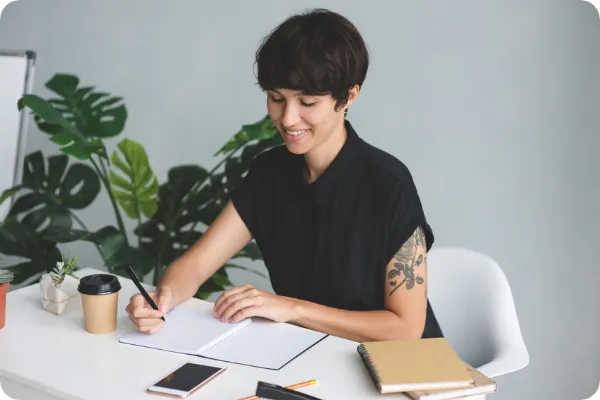 event planner with tattoos writes meeting notes in a journal