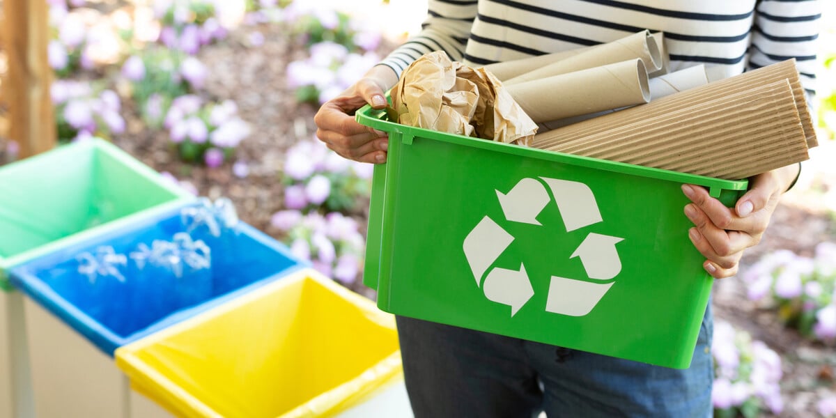 a person holding a recycling bin with paper goods inside
